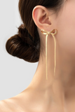 long gold herringbone bow earrings on a woman's ear.