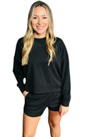 Woman wearing a black long sleeve crewneck shirt with matching black shorts.