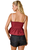 A woman shown from the back wearing a burgundy peplum camisole top with thin white straps and dark denim shorts against a white background.