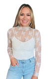 Woman wearing a white long sleeve mesh shirt with lace detail. It is styled with light denim jeans 