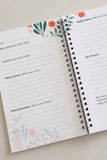 An open spiral-bound journal with printed reflection prompts on the pages, including 'Bible Passage or Topic,' 'Purpose of My Study,' 'Observations,' and 'Interpretations,' decorated with floral illustrations in coral, orange, and muted green on a light neutral background.