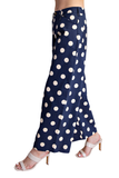 A person wearing navy blue wide-leg pants with a white polka dot pattern, paired with beige heeled sandals, shown from the waist down against a plain white background.