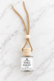 A car diffuser bottle with a white label reading 'NOBLE KNIGHT' and 'THE NOBLE AROMA COMPANY,' suspended from a braided gold-and-white cord with a round wooden bead and stacked wooden diffuser sticks, photographed on a white marble surface.