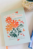 A book titled 'Unfiltered Devotions for Women' with a pale sage green cover, decorated with orange flowers and green leaves, resting on a light marble surface next to a floral ceramic cup.