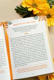 An open devotional spread on a surface, showing the title 'GROWTH IN THE LORD' and scripture text, with orange flowers placed around it.