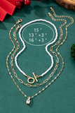 A set of three necklaces featuring a pearl chain choker with a toggle closure, a fine paperclip chain, and a delicate twisted chain with a CZ pendant on a green background showing the necklaces measurements. Pearl chain chocker is 15 inches long, the paperclip chai is 13 inches with a 3 inch extender, the twisted chain is 16 inches long with a 3 inch extender 