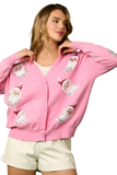 Woman wearing a pink button down cardigan with sequin Santa detailing on the front of the cardigan 