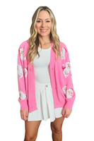 Woman wearing a white shirt and skirt with a pink button down cardigan over. Pink cardigan has sequin Santa faces on the front 