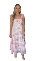 Woman wearing a white and pink floral maxi dress with a square neck line. Dress is an empire waist with crochet detailing along the top and straps. 