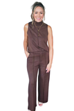 A woman modeling a sleeveless, high-neck, wide-leg jumpsuit in a dark brown color, standing against a solid white background.