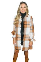 woman wearing a plaid button down shacket over a black turtle neck sweater and black leather skirt. Plaid pattern is composed of white, black, camel and orange colors 