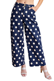 A model wearing navy blue wide-leg cropped pants with a white polka dot pattern, paired with white heeled sandals, shown against a plain white background.