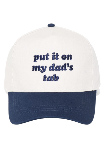 Cream and navy trucker hat with snapback closure, featuring embroidered navy text on the front that reads, “put it on my dad’s tab.”