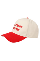side view of a 2 tone 5 panel trucker hats, hats are embroidered with "put it on my dads tab" on the front panel. Hat is ivory with red stitching and bill