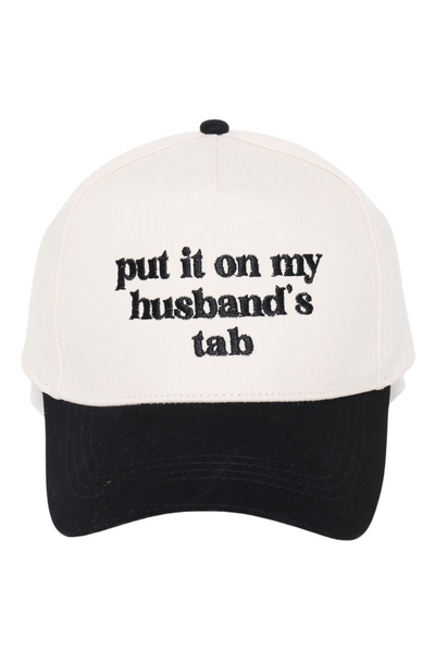 white baseball cap with a black bill. Hat says "put it on my husbands tab" in black thread embroidery on the front 