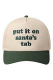 Cream and green trucker hat featuring embroidered green text on the front that reads, “put it on santa’s tab.”