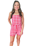 Woman wearing a red and white gingham summer romper with scallop trim detailing at the waist and hem, adjustable straps, and a fitted Americana-inspired silhouette.