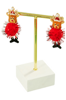 Christmas earrings on a gold T style earring stand. Earrings have reindeer heads wearing a Santa hat, a red glittery pom pom body and black dangling boots 