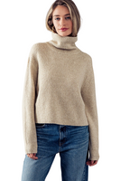Woman wearing an oatmeal colored ribbed turtleneck sweater with jeans 