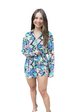 Woman wearing a long sleeve button down romper that looks like a dress. She is holding up the overlay to show the shorts underneath 