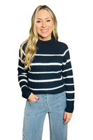 woman wearing a navy high-neck sweater with white stripes. Sweater is paired with light blue wide-leg jeans 