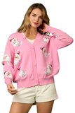 Woman wearing a pink button down cardigan with sequin Santa detailing on the front of the cardigan 