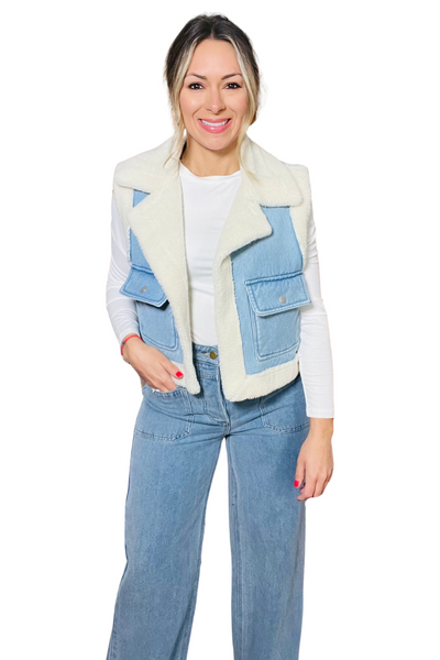 woman wearing a white long sleeve shirt and light denim pants with a white sherpa lined denim vest. The vest has 2 cargo pockets with a flap and button closure. 