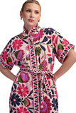 A woman modeling a short-sleeved, high-neck dress with a colorful floral and paisley print on a light pink base. The dress features a tie belt at the waist and is photographed against a solid white background.