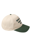 side view of a cream and green trucker hat featuring embroidered green text on the front that reads, “put it on santa’s tab.”
