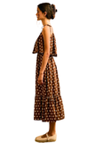 A woman shown in profile wearing a brown sleeveless midi dress with white polka dots, ruffled shoulder details, and a tiered skirt, paired with tan flat shoes against a plain white background.