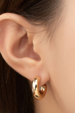 A pair of gold hollow tube puffy hoop earrings with a polished finish, measuring 0.75 inches in diameter on a woman's ear