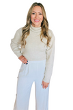 Woman wearing an oatmeal colored ribbed turtleneck sweater with linen pants