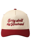 5 panel 2 tone (ivory and maroon) trucker style hat that has "Sorry About My Husband" Embroidered on the front. The embroidery is in maroon stitching that matches the bill.
