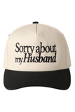 Cream and black trucker hat with black embroidered text reading “Sorry about my husband” on the front panel.