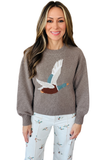 A woman wearing a taupe knit sweater with a large embroidered duck motif on the front, paired with white patterned pants, against a plain white background.
