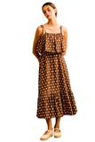 A woman modeling a brown sleeveless midi dress with white polka dots, featuring thin shoulder straps, a ruffled chest detail, and a tiered skirt, paired with beige espadrille flats against a plain white background.