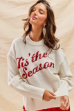 Model wearing a white Tis The Season Sequin Sweater with red sequin lettering, paired with red sequin skirt, festive Christmas outfit idea.
