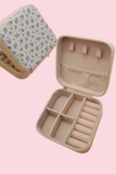 Open travel jewelry organizer case showing compartments, ring slots, necklace hooks, and soft interior lining on pink background
