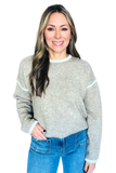 A woman wearing a light heather gray knit sweater with white contrast trim at the crew neck, cuffs, and hem, paired with blue jeans, against a solid white background.