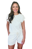 Woman wearing an ivory matching lounge set featuring a relaxed crew neck top and elastic waist shorts with front patch pockets, styled as a casual two-piece outfit for everyday wear.