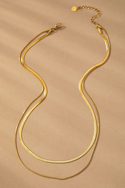 Layered gold necklace, shorter chain is a gold herringbone chain, longer chain is a thin snake chain. Necklaces are joined by one clasp