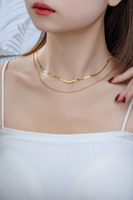 woman wearing a gold layered chain necklace. Shorter chain is a herringbone chain, longer chain is a snake chain.