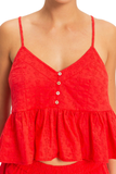 A close-up of a model wearing a bright red eyelet camisole top with thin straps, a V-neckline, and a button-down front.