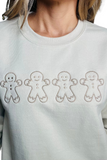 Upclose photo of a tan sweatshirt with 4 embroidered gingerbread cookies on the front center 