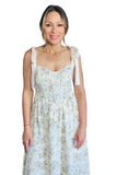 Woman wearing a maxi dress with a floral print. Dress has a corset style top with satin tie straps