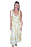 A woman modeling a sleeveless maxi dress with a yellow and green floral print on a cream background, featuring lace-up shoulder straps, against a plain white background.