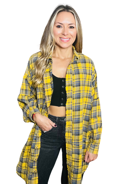 Woman wearing a mineral washed oversized flannel shirt with a cropped black top and black jeans. Flannel is a yellow. blue and gray black checkered pattern. 