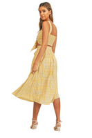 Woman looking over her shoulder. woman wearing a yellow gingham pattern set. Set is a cropped top that ties in the front with a midi skirt that has a belt 