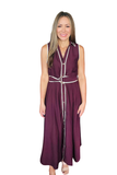 A woman modeling a sleeveless, deep plum purple maxi dress with white piping and button details, set against a plain white background.