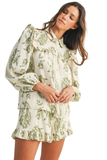 Woman wearing an olive green floral matching set featuring a ruffle trim babydoll blouse with puff sleeves, Peter Pan collar, and flowy ruffle hem shorts in lightweight gauze fabric.